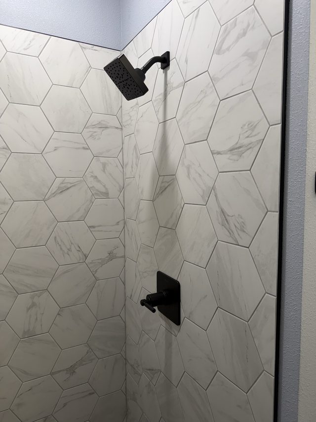 white marble hexagon tile shower with black showerhead and valve