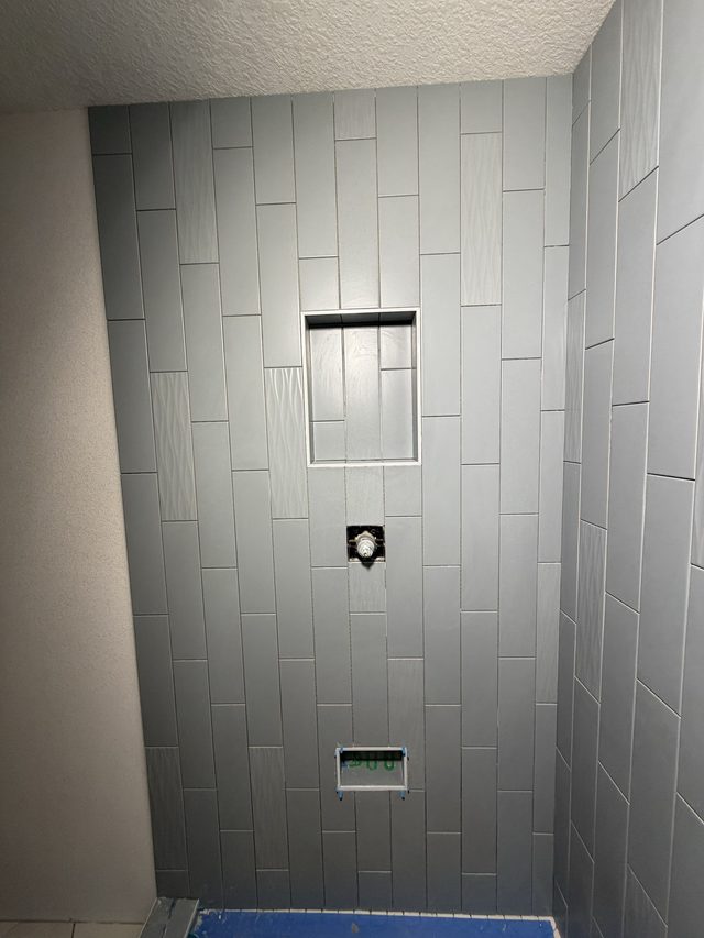 gray tile shower wall in progress with niche and valve