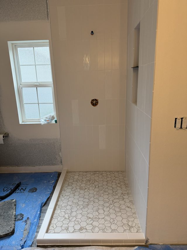 white tile shower with hex mosaic floor, niche and window