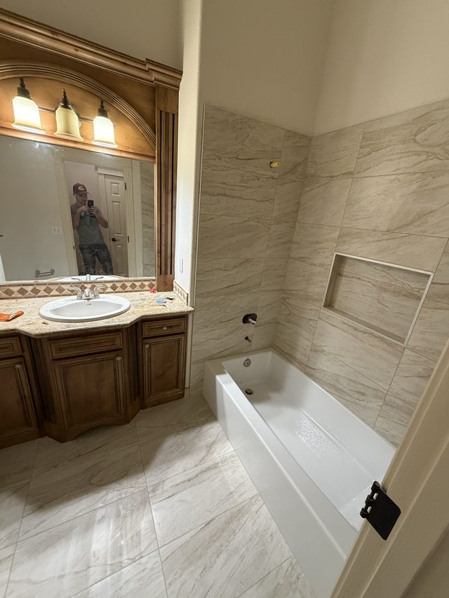 bathtub with tiled surround and niche, wood vanity with mirror and sconces