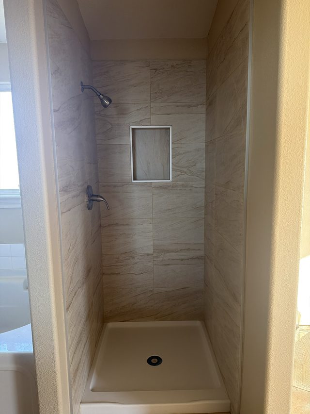 stand-up shower with stone-look tile walls, niche, shower pan and fixtures