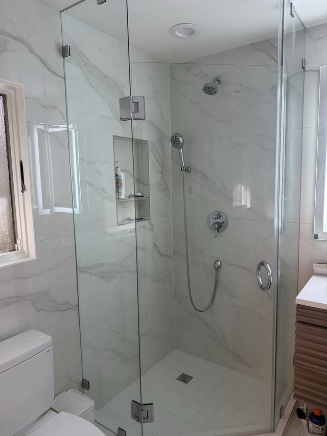 glass walk-in shower with white marble-look tile, niche, toilet