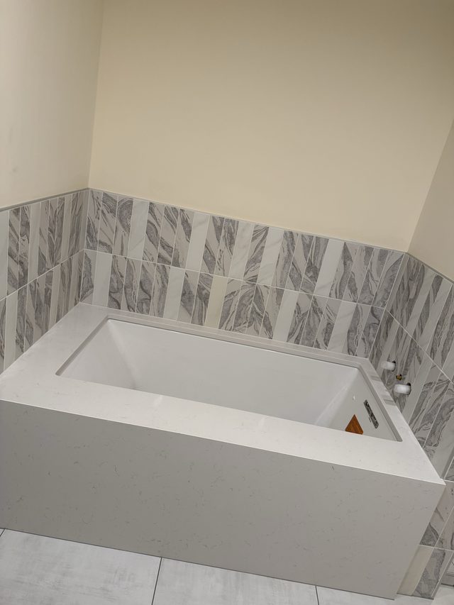 bathtub with gray marble-look tile surround and quartz apron
