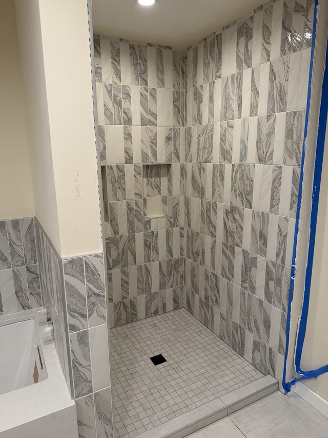 walk-in shower with gray patterned tile, niche, mosaic pan, tub adjacent