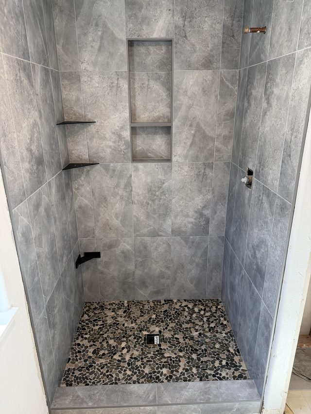 walk-in shower with gray tile, niche, shelves, pebble stone floor pan
