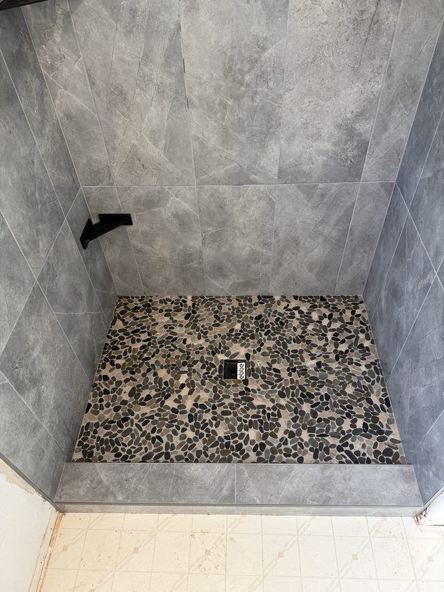 walk-in shower with gray tile and pebble stone mosaic floor pan
