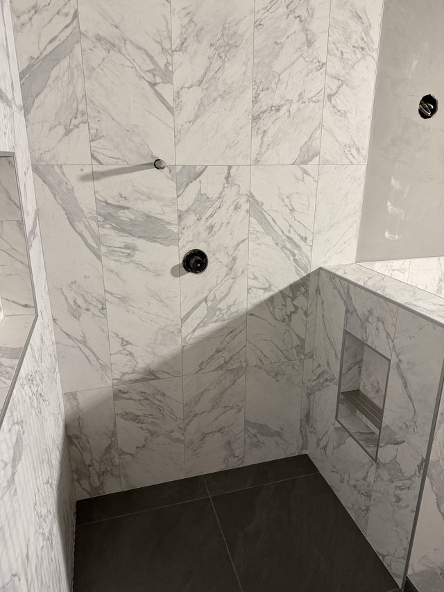 marble-tiled shower with valve and niche, dark floor tile