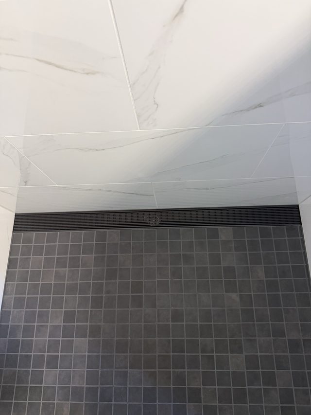 marble wall tile with dark mosaic shower floor and linear drain