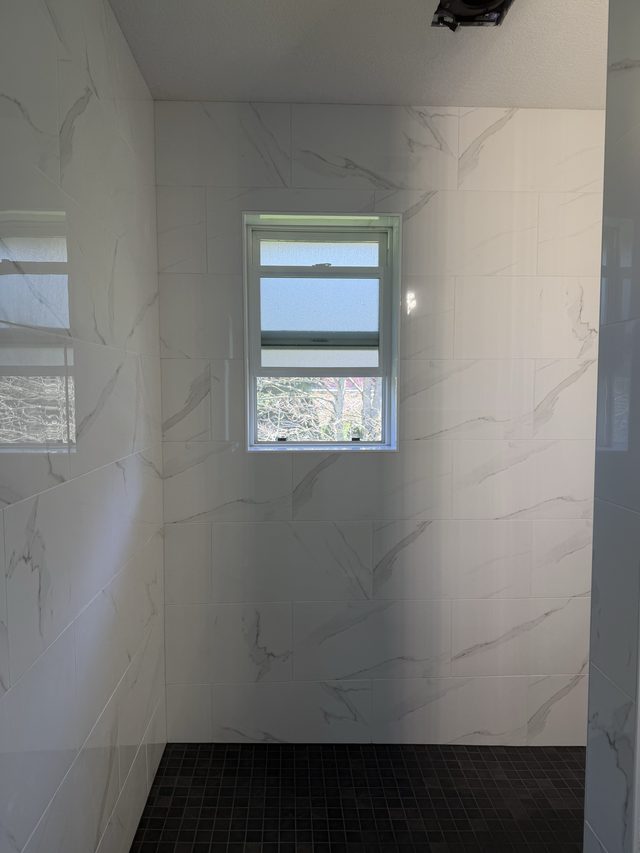 marble-tiled walk-in shower with window and dark mosaic floor