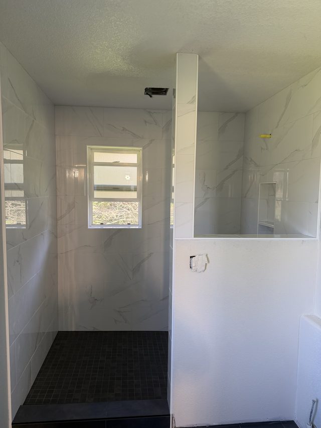 marble walk-in shower with window and dark mosaic floor