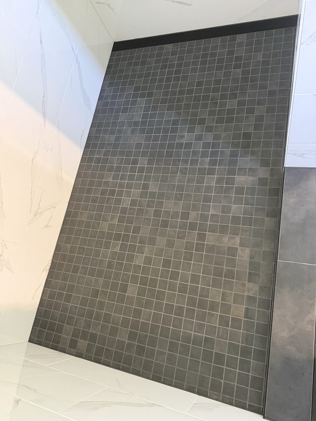 dark mosaic shower floor sloped against marble walls