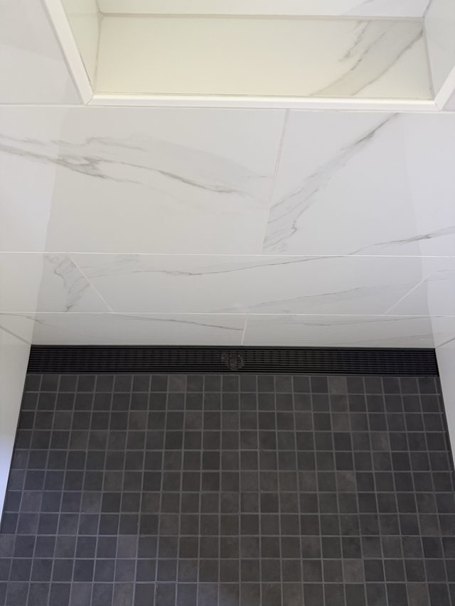 marble walls with dark mosaic shower floor and linear drain
