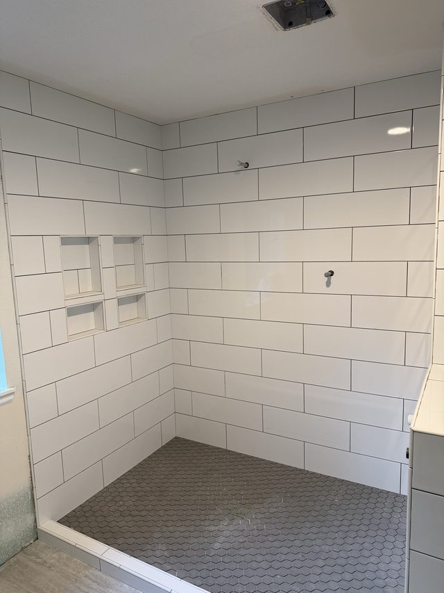 white subway tile shower with shelf niches and gray hex tile floor