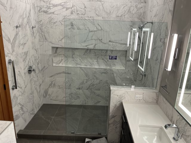 marble shower with glass enclosure, vanity and sink visible