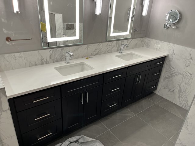 black double vanity with sinks, lit mirrors, marble backsplash