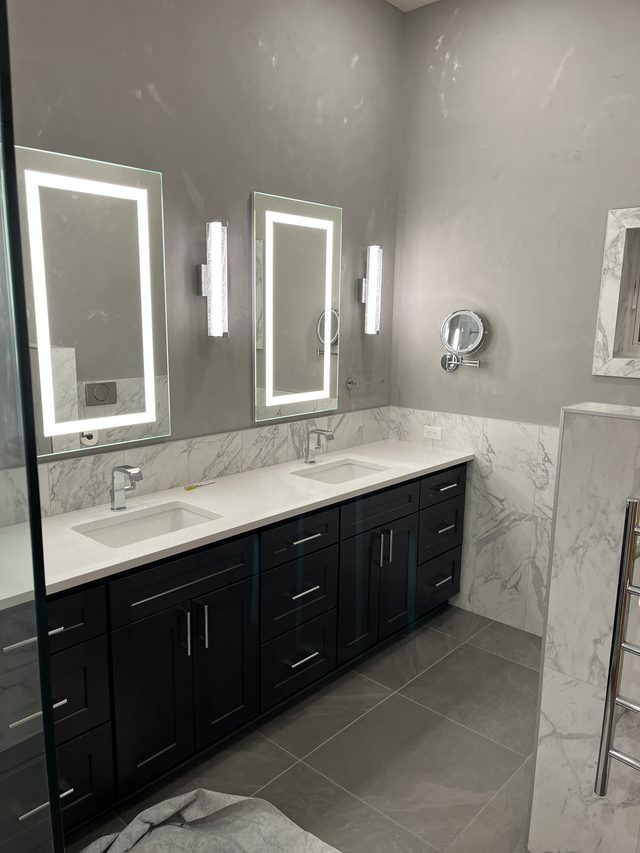 double vanity with sinks and lit mirrors, marble wainscot