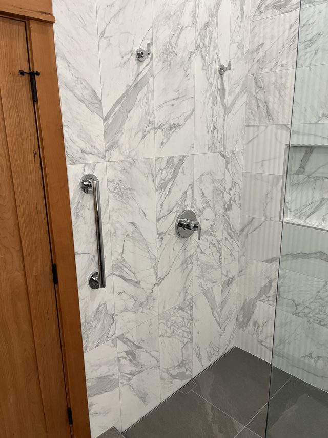 marble tile shower with grab bar and chrome fixtures