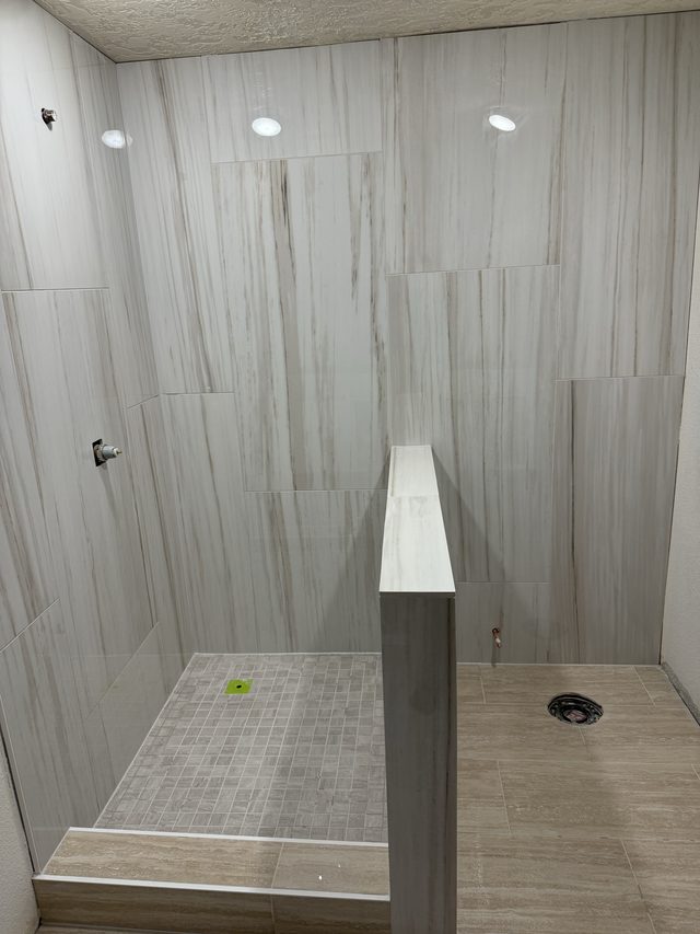 vein-cut tile walk-in shower with mosaic pan and pony wall