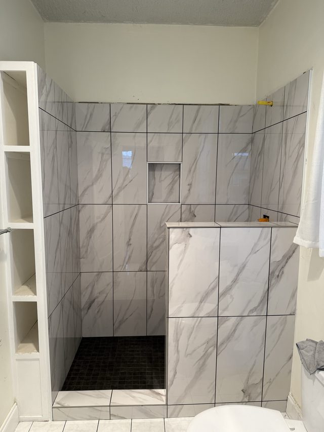 marble-look tiled shower with niche, pony wall, toilet visible