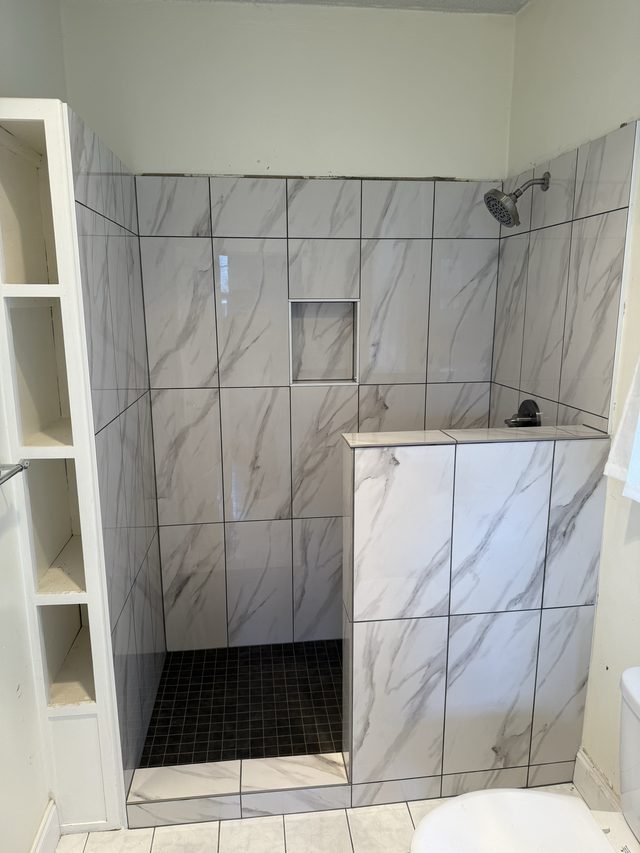 marble-look tiled shower with showerhead and niche