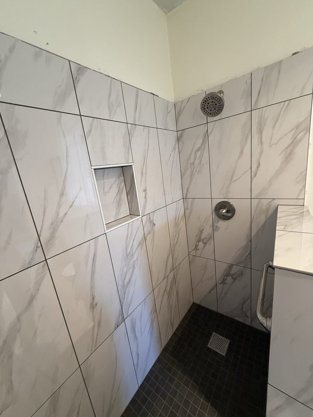 marble-look tiled shower with niche and dark mosaic floor