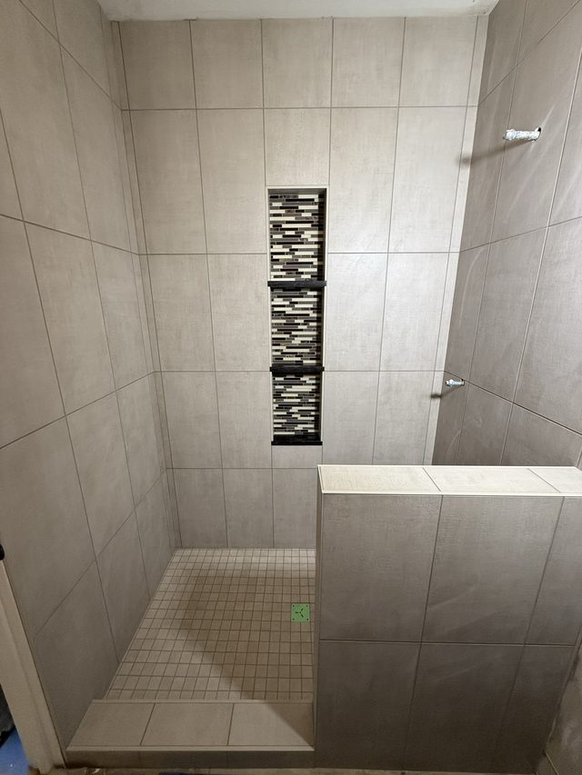 tiled walk-in shower with linear mosaic niche and half wall