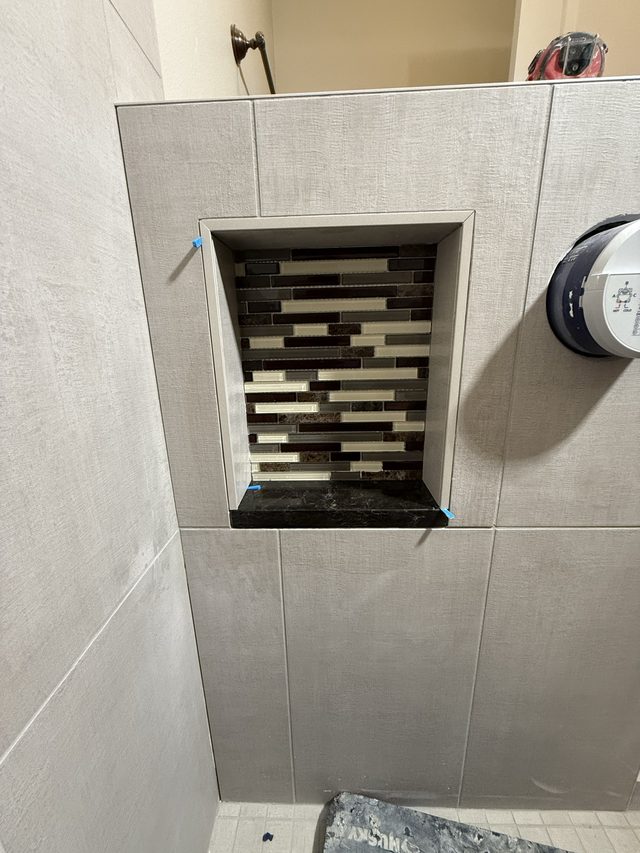 shower wall tile with dark linear mosaic niche and showerhead