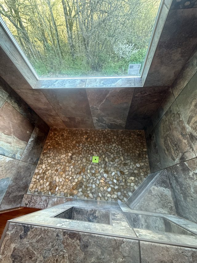 stone tile shower with pebble floor and window seat