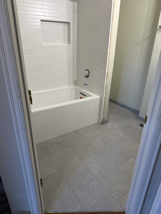 bathtub with subway tile surround and gray tile bathroom floor