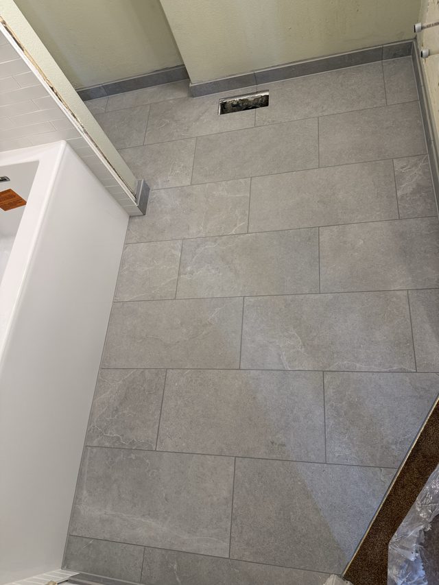 gray tile bathroom floor beside tub with linear drain, inside bath
