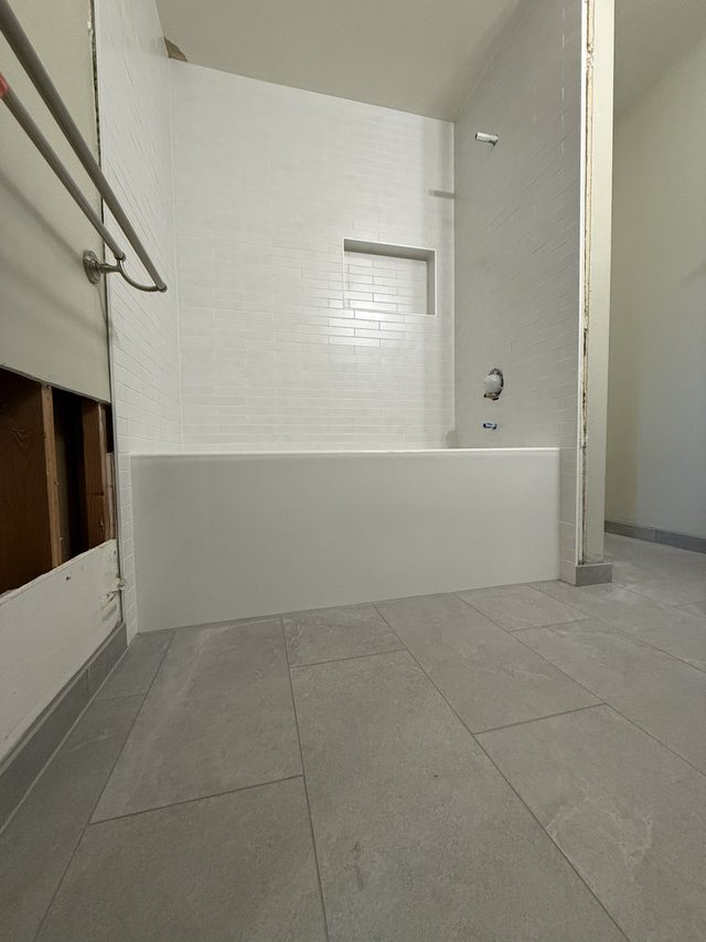 bathtub with white subway tile surround, niche, tile floor