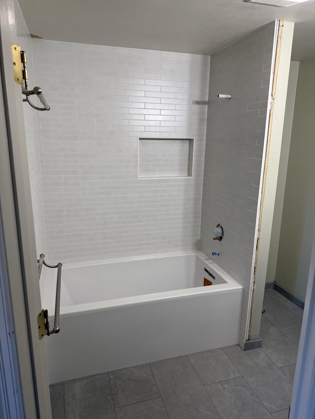 white bathtub with white subway tile shower surround and niche