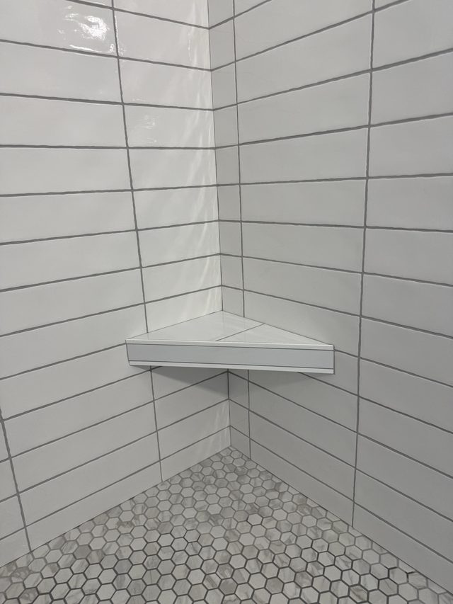 white tile shower with corner shelf and hexagon mosaic floor