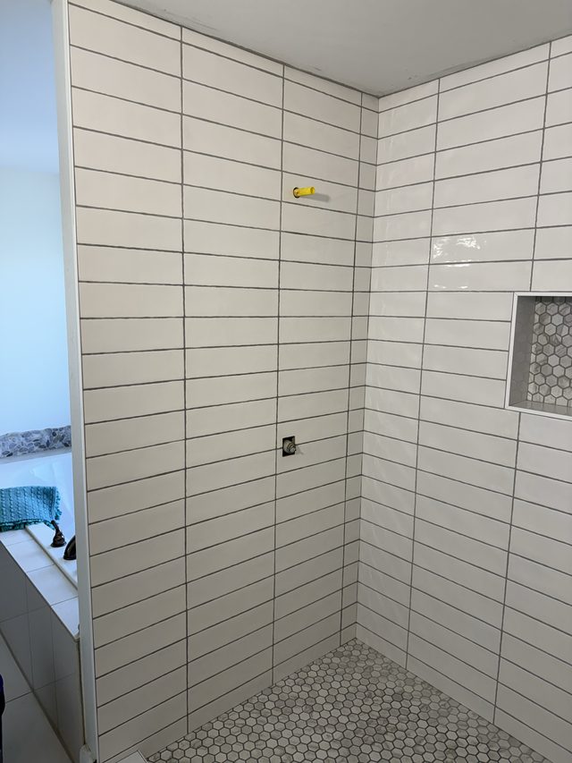 white tile shower wall with niche, tub at left, hex floor