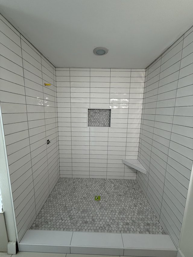 white tile walk-in shower with niche, corner bench, hex floor