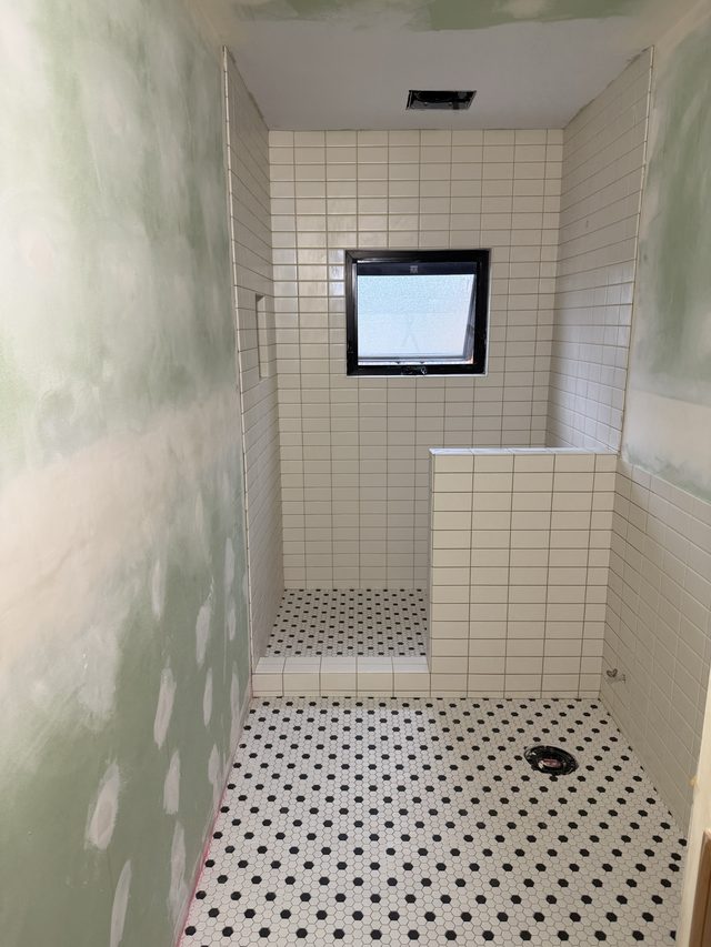 white subway tile shower with window and mosaic floor