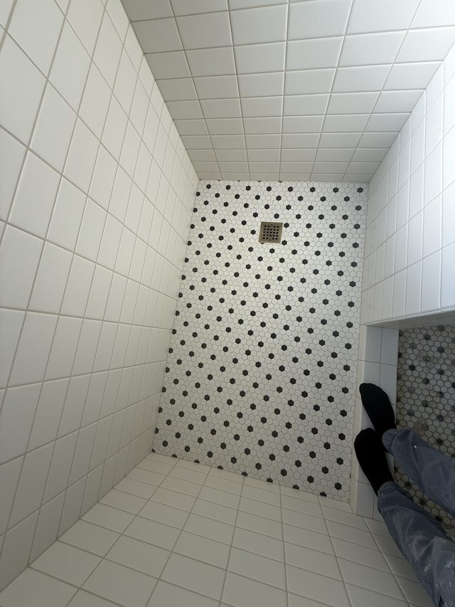 white tiled shower with B&W mosaic floor and drain