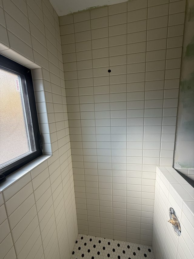 tiled shower wall with window and mosaic floor