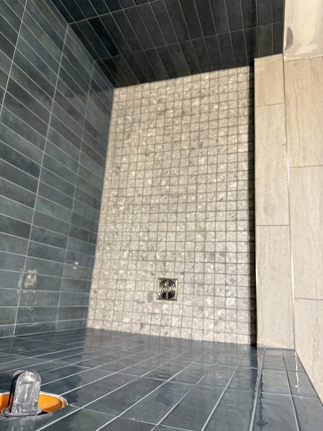 shower with dark and light mosaic tile walls and floor drain