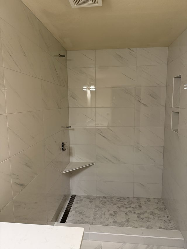 marble-tile walk-in shower with corner seat and mosaic pan