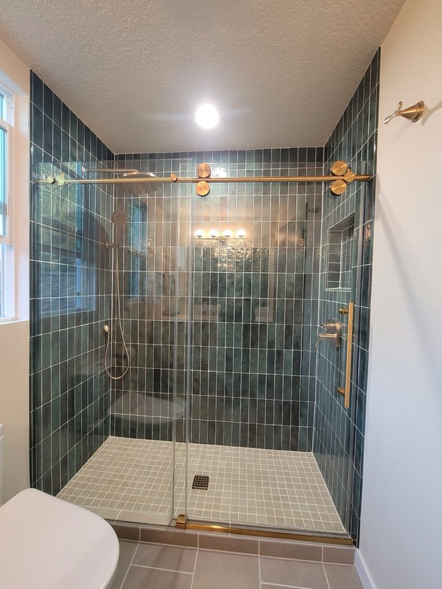 teal vertical-tile walk-in shower with gold hardware and glass door