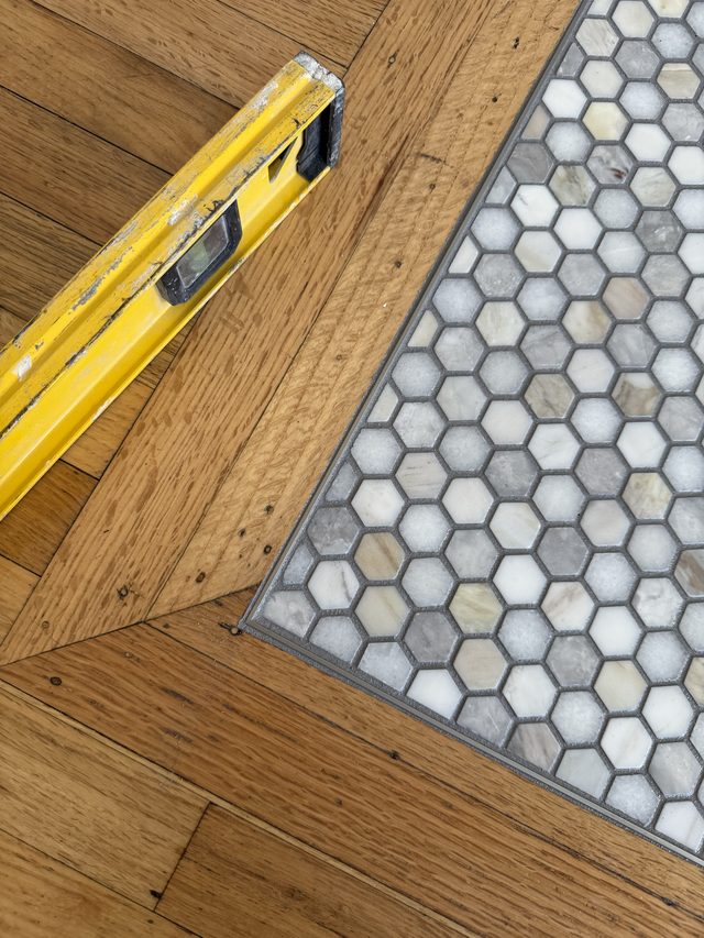 hex mosaic tile meeting herringbone hardwood floor, level on floor