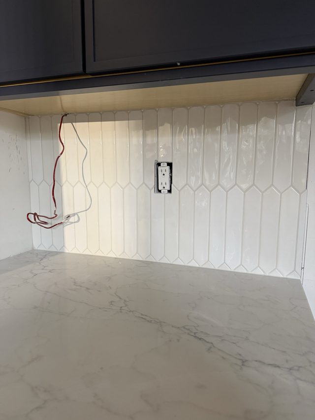 white vertical picket tile backsplash with outlet under dark cabinets, marble countertop