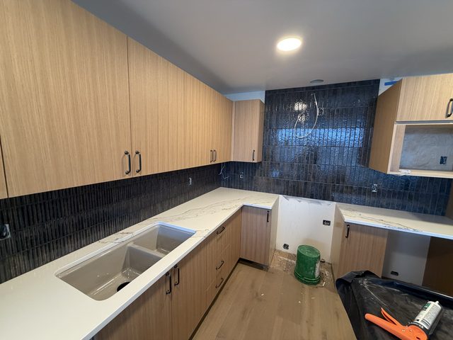 kitchen with light cabinets, quartz counter, dark backsplash and undermount sink