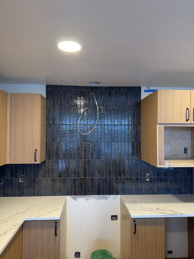 kitchen with dark blue vertical tile backsplash, marble counters and cabinets