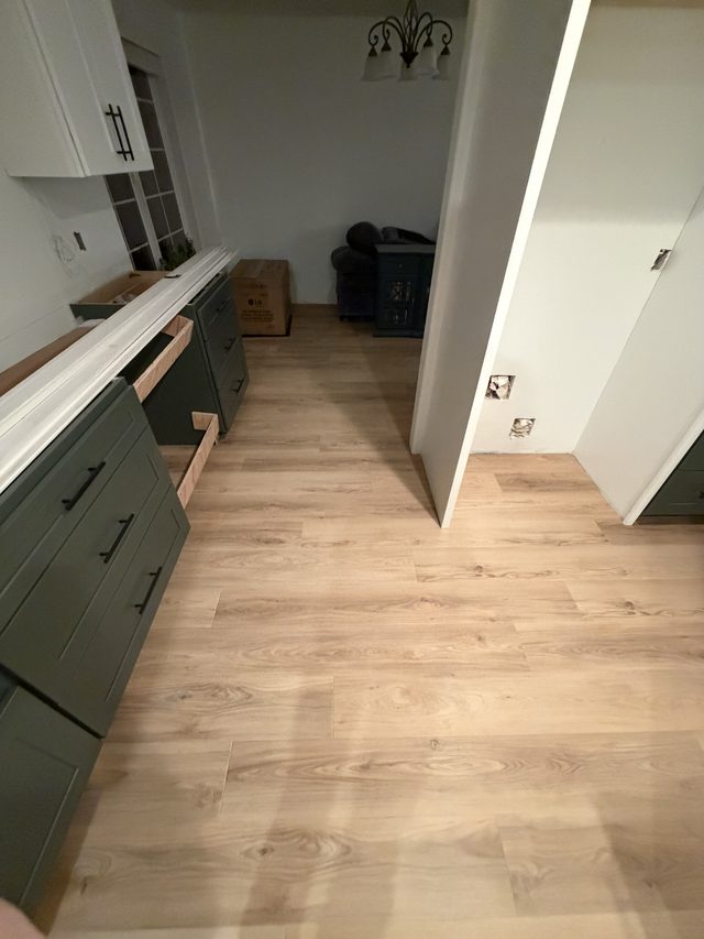 green kitchen cabinets with new vinyl plank flooring, chandelier in adjoining dining area