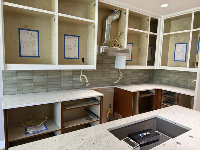 kitchen with range hood, backsplash, countertops and island sink