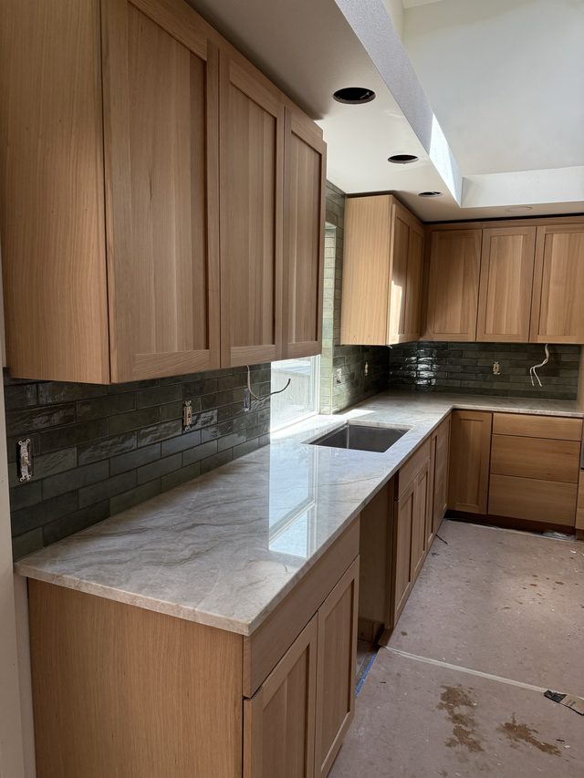 oak cabinets, marble countertops, green tile backsplash and kitchen sink