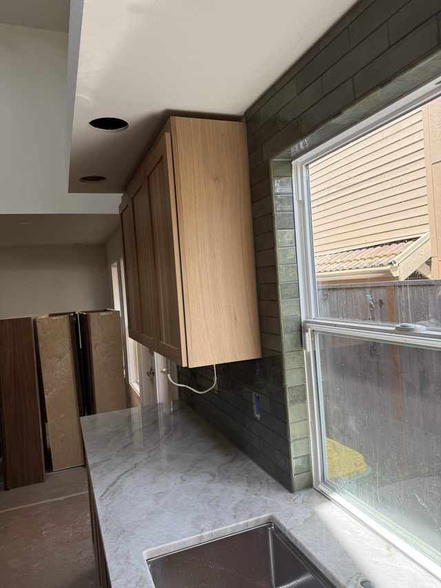 kitchen upper cabinet, dark tile backsplash and sink by window