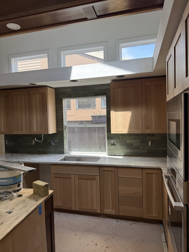 oak kitchen cabinets, green backsplash, marble counters and cooktop